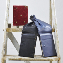 A medieval style velvet book and two leather girdle books displayed on a ladder